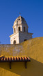 bell tower against a blue sky with yellow wall in foreground