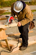 Construction worker cutting piece of lumber with saw