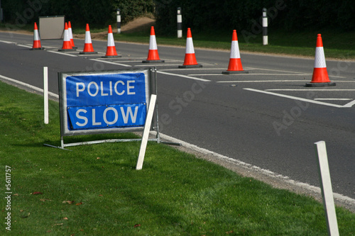 Photo: blue police slow sign with warning cones in the road blue police slow sign with warning cones in the road