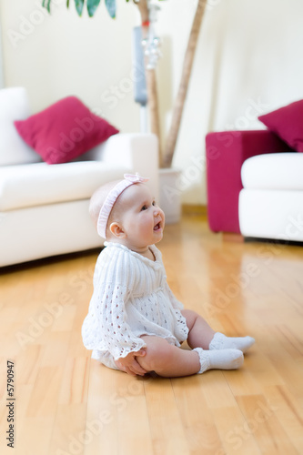 Happy eight month old baby girl seated on a hardwood floor