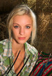 beautiful blonde lady holding hayfork close to her face 