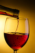 Red wine pour into glass close-up over yellow background