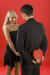 Young man in suit is hiding gift before woman