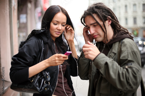 Photo: Young couple listening to a portable music player on a street Young couple listening to a portable music player on a street