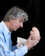 Mature man looking in an empty skull with brain in his hand.