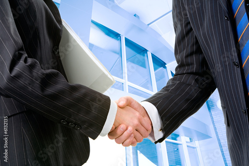 Two partners shaking hands at meeting in front of building