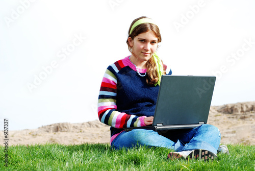 Photo: young girl is working on laptop at outdoor location young girl is working on laptop at outdoor location