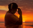 Indian lady in saree doing the namaste greeting at sunset