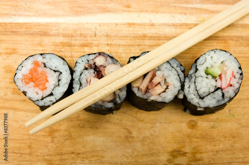 Photo: Various sushi rolls on cutting board with chopsticks. Various sushi rolls on cutting board with chopsticks.