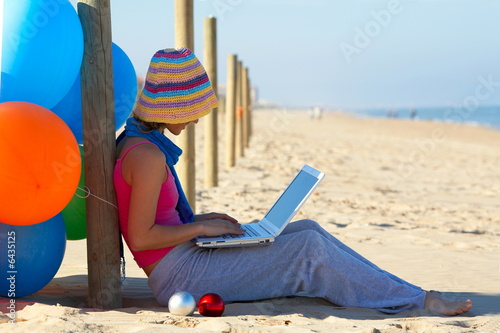 girl with colorful balloons using a laptop on the beach girl with colorful balloons using a laptop on the beach