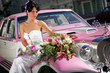 Bride sat on pink cadillac limousine smiling