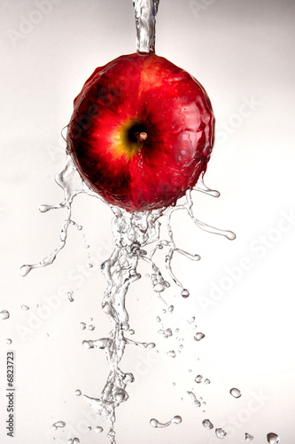 Photo: Water pouring and splashing over a red delicious apple on white Water pouring and splashing over a red delicious apple on white
