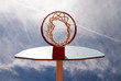 Basketball hoop shot from underneath in a cloudy blue sky.