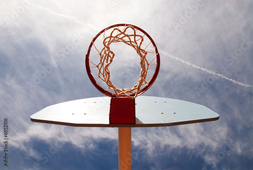 Photo: Basketball hoop shot from underneath in a cloudy blue sky. Basketball hoop shot from underneath in a cloudy blue sky.