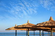 straw umbrellas on blue sky and sea with pier.