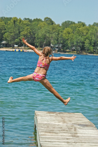 Photo: Young Girl Jumps Off Dock into Lake Extending Arms and Legs Young Girl Jumps Off Dock into Lake Extending Arms and Legs