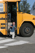 Happy boy with glasses getting off the yellow school bus 