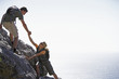 Photo: Couple climbing rock in bright sunlight, man assisting woman, side view, sea in background Couple climbing rock in bright sunlight, man assisting woman, side view, sea in background