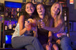 Three young women sitting on a bar counter, toasting the camera