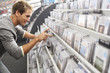 Photo: Young man sifting through CDs in record shop, bending down, smiling, side view (tilt) Young man sifting through CDs in record shop, bending down, smiling, side view (tilt)