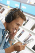 Photo: Young man wearing headphones, listening to CDs in record shop, smiling, close-up, side view (tilt) Young man wearing headphones, listening to CDs in record shop, smiling, close-up, side view (tilt)