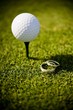 Wedding rings lying on a golf green next to a ball on tee