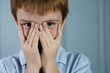 boy with ginger hair playing peek a boo through fingers