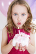 little girl blowing out candle on miniature birthday cake