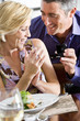 Mature man proposing to mature woman at dinner table, smiling, woman looking at engagement ring