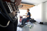 Photo: Teenage boy (16-18) playing drums in garage, looking at friend playing electric guitar in foreground Teenage boy (16-18) playing drums in garage, looking at friend playing electric guitar in foreground
