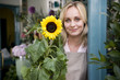 Woman florist standing at the entrance to her shop, holding a sunflower