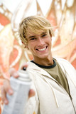 Photo: Portrait of a young man holding a spray can in front of a wall covered in graffiti Portrait of a young man holding a spray can in front of a wall covered in graffiti
