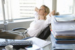 Photo: Young businesswoman leaning back in chair in office, arms behind head, eyes closed, files on desk in foreground Young businesswoman leaning back in chair in office, arms behind head, eyes closed, files on desk in foreground