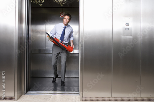Foto: Young businessman holding fire extinguisher in lift Young businessman holding fire extinguisher in lift