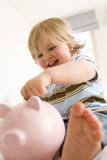 Photo: Baby boy (9-12 months) putting coin in piggy bank, smiling, low angle view (differential focus) Baby boy (9-12 months) putting coin in piggy bank, smiling, low angle view (differential focus)