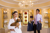 Photo: Young woman shopping with dog in glamorous designer handbag boutique, male shop assistant carrying bags, smiling, portrait Young woman shopping with dog in glamorous designer handbag boutique, male shop assistant carrying bags, smiling, portrait