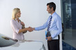 Photo: Car salesman shaking hands with female customer in showroom, man holding brochure, smiling, profile Car salesman shaking hands with female customer in showroom, man holding brochure, smiling, profile