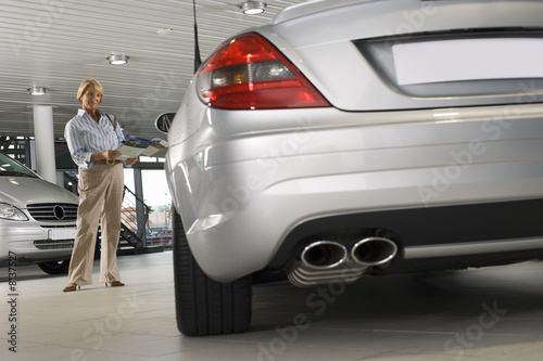 Photo: Senior woman looking at new silver convertible car in large showroom, holding brochure, smiling (surface level) Senior woman looking at new silver convertible car in large showroom, holding brochure, smiling (surface level)