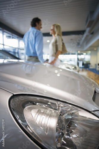 Photo: Couple holding hands in large showroom, focus on bonnet of new silver car in foreground, side view Couple holding hands in large showroom, focus on bonnet of new silver car in foreground, side view