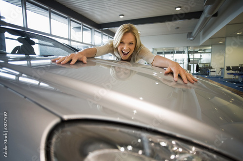 Photo: Excited woman embracing bonnet of new silver car in large showroom, smiling, portrait (surface level) Excited woman embracing bonnet of new silver car in large showroom, smiling, portrait (surface level)