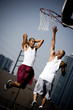 Foto: Two Young African American man jumping with a basketball on an urban basketball court Two Young African American man jumping with a basketball on an urban basketball court