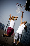 Foto: Two Young African American man jumping with a basketball on an urban basketball court Two Young African American man jumping with a basketball on an urban basketball court