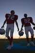 Photo: Two American football players leaving pitch at sunset, side by side, front view (surface level, backlit) Two American football players leaving pitch at sunset, side by side, front view (surface level, backlit)