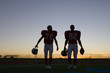 Photo: Two American football players leaving pitch at sunset, side by side, front view (backlit) Two American football players leaving pitch at sunset, side by side, front view (backlit)