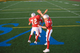 Photo: Three American football players, in red football strips, celebrating touchdown on pitch during competitive game, doing high-fives, elevated view Three American football players, in red football strips, celebrating touchdown on pitch during competitive game, doing high-fives, elevated view