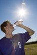 Photo: Sportsman drinking water from bottle on pitch, profile, low angle view (lens flare, tilt) Sportsman drinking water from bottle on pitch, profile, low angle view (lens flare, tilt)