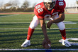 Photo: American football running back, in red football strip, crouching with ball in scrimmage line during competitive game, front view American football running back, in red football strip, crouching with ball in scrimmage line during competitive game, front view
