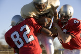 Photo: Determined American football player running with ball during competitive game, opposing players attempting to tackle Determined American football player running with ball during competitive game, opposing players attempting to tackle