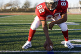 Photo: American football running back, in red football strip, crouching with ball in scrimmage line during competitive game, front view American football running back, in red football strip, crouching with ball in scrimmage line during competitive game, front view