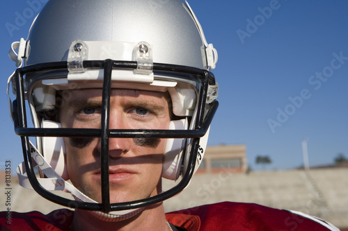 Photo: American football player wearing football strip and protective helmet, standing on pitch, close-up, front view, portrait American football player wearing football strip and protective helmet, standing on pitch, close-up, front view, portrait